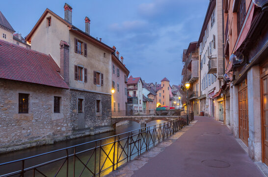 Cobblestone street with historic buildings and glowing street lamps in Annecy, France, during blue hour.