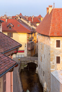 Red tiled rooftops, stone buildings and a narrow canal in the historic center of Annecy, France.
