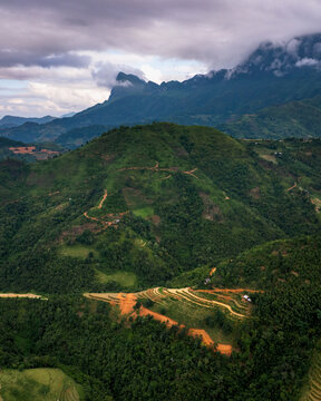 Aerial view of Nham La View featuring lush green mountains, terraced fields, and winding dirt paths under a cloudy sky in Mau Due, Tuyen Quang, Vietnam.