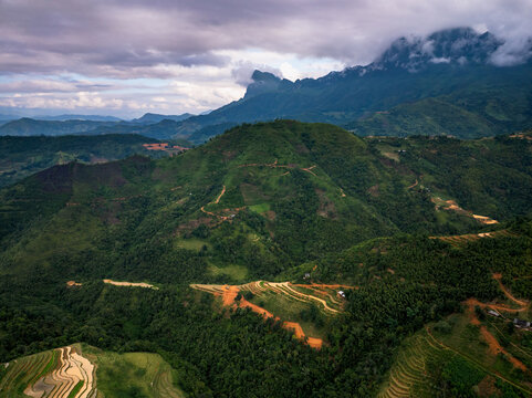 Aerial view of Nham La View featuring lush green mountains, terraced rice fields, and winding dirt paths under a cloudy sky in Mau Due, Tuyen Quang, Vietnam.