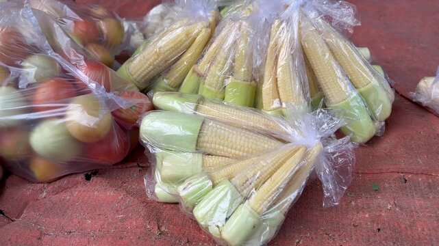 Fresh baby corn and tomatoes packed in plastic bags at traditional market