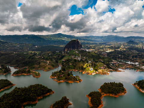 Aerial view of the massive monolith La Piedra rising above the surrounding lush green hills and the winding waters of the Guatape reservoir in La Piedra, Antioquia, Colombia.