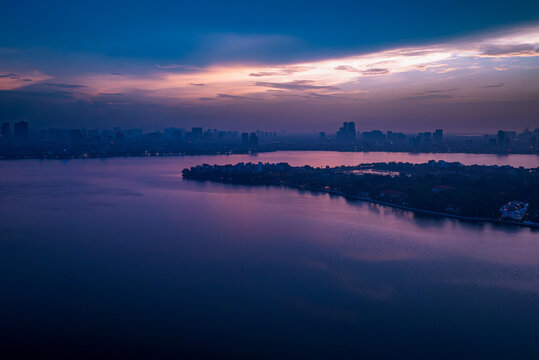 Aerial view of West Lake at dusk with the city skyline of Hanoi in the background, reflecting purple and blue twilight colors on the water surface in Hanoi, Ha Noi, Vietnam.