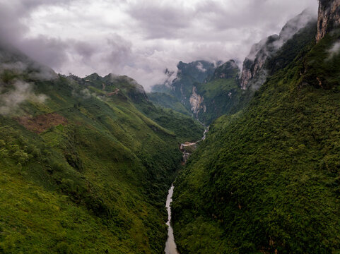 Aerial view of the Ha Giang Loop featuring lush green mountains, a winding river flowing through the valley, and low-hanging clouds in Dong Van, Tuyen Quang, Vietnam.