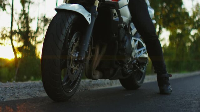 Powerful sport motorcycle idling on rural asphalt road at sunset with rider in black gear preparing for evening ride through scenic forest landscape