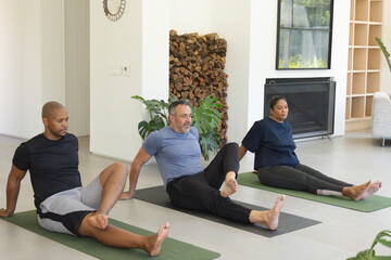 Fototapeta premium Diverse group wearing athletic wear stretching legs on yoga mats in sunny living room with firewood