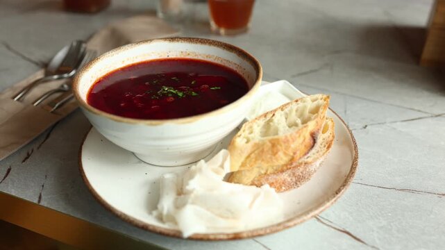 A cook prepares borscht in a Ukrainian cafe. A bowl of red soup is served with fresh bread. The process shows ingredients and the final dish on the table.