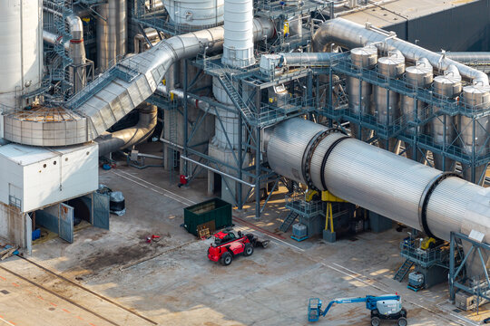 Aerial view of a modern wood processing facility featuring industrial pipes, metal silos, and machinery with a red tractor and blue aerial work platform on the concrete ground in Poland.