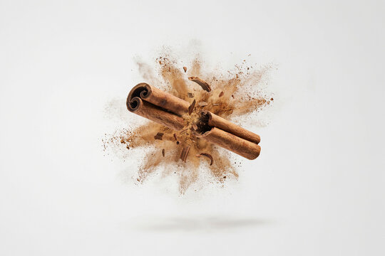Cinnamon sticks with ground cinnamon powder explosion on white background, aromatic spice concept for baking, cooking and food packaging design