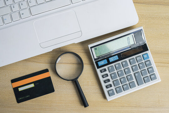 Top View of Calculator Credit Card and Magnifying Glass Beside Laptop