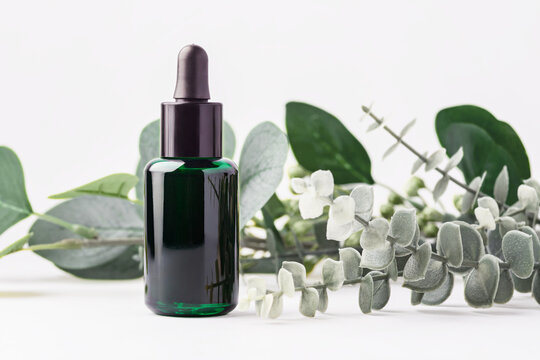 Green essential oil dropper bottle with green leaves decoration on white background, natural skincare, wellness, and aromatherapy