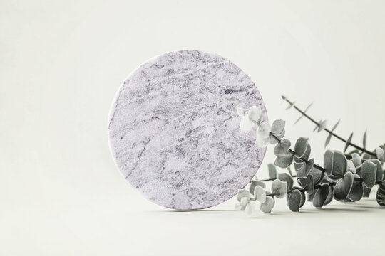 Empty round marble podium with green leaves on light green background for product display, cosmetic, perfume, jewelry, or skincare product mockups and presentations