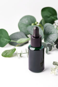 Dark green essential oil dropper bottle with green leaves decoration on white background, natural skincare, wellness, and aromatherapy
