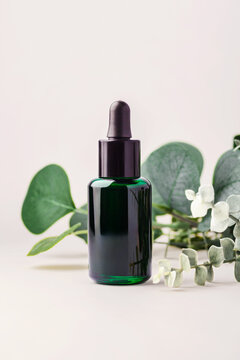 Dark green ssential oil dropper bottle with green leaves decoration on beige background, natural skincare, wellness, and aromatherapy