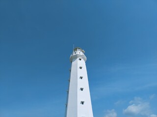 White lighthouse stands tall against clear blue sky © rico