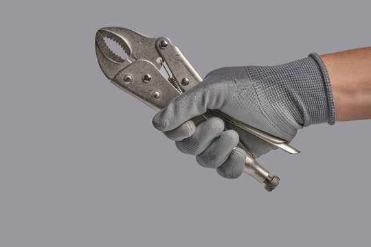 Hand in protective grey glove holding metallic locking pliers isolated against grey studio background.