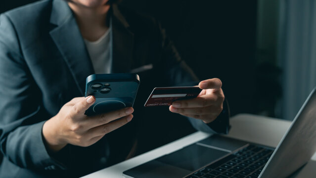 Business person using mobile phone and credit card for online payment or digital transaction in modern office workspace with laptop