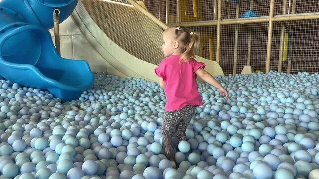 Young girl playing in a colorful ball pit at an indoor play center, active childhood, joyful recreation, family leisure, playful learning.