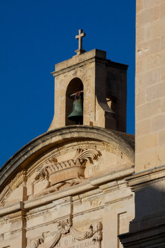 Stone bell tower with a bronze bell and christian cross under a bright blue sky