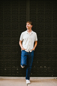 Young man in striped shirt leaning against a wall