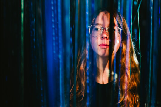 Young woman with glasses looks through neon light reflections