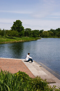 Young man sits alone by a calm lake in a park