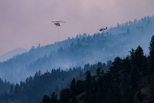 Two helicopters fight a smoky mountain wildfire at twilight