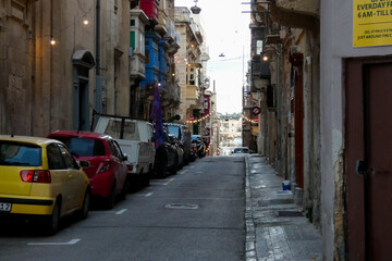 Fototapeta premium Narrow street with parked cars leading to the sea in valletta, malta