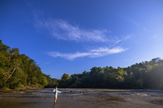 Man fly fishing in a wide river on a sunny day