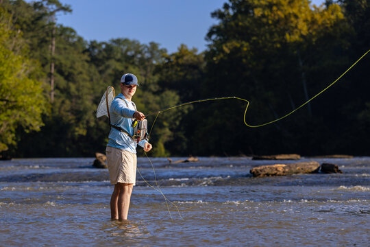 Young man fly fishing in a sunny river