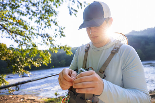 Fly fisherman rigging tackle by a river at sunrise