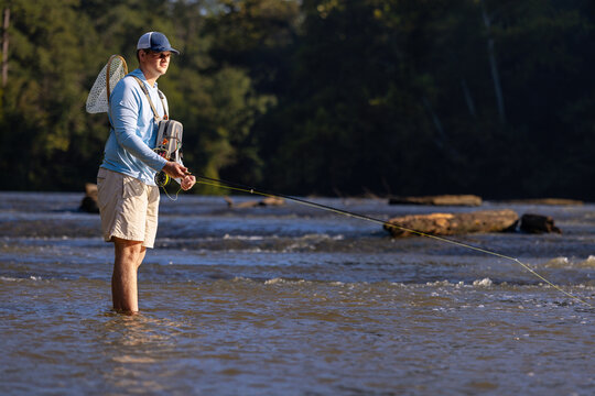 Young man standing in a river while fly fishing