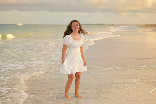 Happy teenage girl in white dress on the beach at sunset