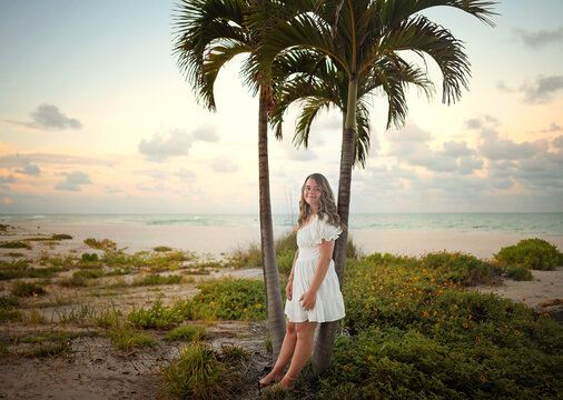 Young woman in white dress by a palm tree on the beach