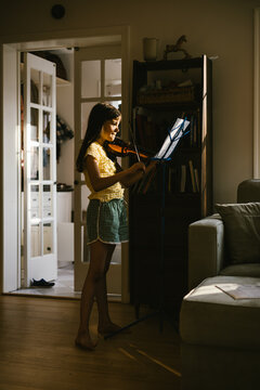 Young girl practices violin in a sunlit room
