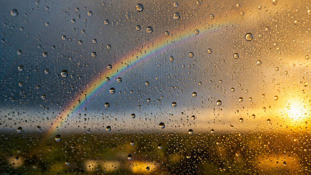 A vibrant rainbow appears through a rain-covered window at sunset, blending dark storm clouds with warm golden light.