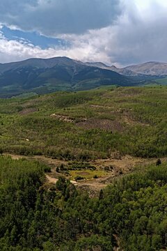 Aerial view of the mountainous landscape near Twin Lakes featuring dense green forests, rolling hills, and dramatic clouds over the peaks in Twin Lakes, Colorado, United States.