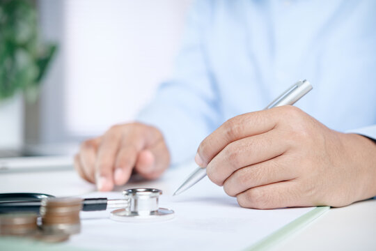 Doctor or health insurance agent signing medical document or healthcare contract, concept of medical cost planning, health insurance coverage, financial protection for medical expenses.