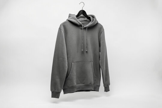 Gray pullover hoodie on hanger against white wall, casual blank sweatshirt with drawstring hood and kangaroo pocket for apparel mockup
