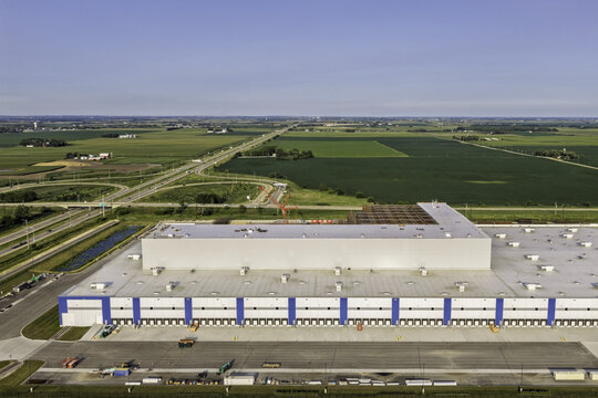 Aerial view of a large data center facility with a flat roof and numerous loading docks, surrounded by expansive agricultural fields and highway infrastructure in DeKalb, Illinois, United States.