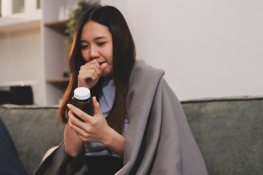 sick asian young woman sneezing into tissue paper while covered with a blanket and sitting on sofa in the living room