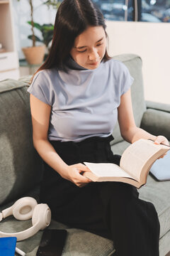 Freelance Asian woman holding mobile phone typing on laptop and working from home. Happy young girl sitting on sofa in living room.