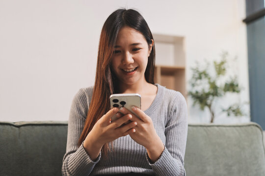 Happy relaxed young woman sitting on couch using cell phone, smiling lady laughing holding smartphone, looking at cellphone enjoying doing online ecommerce shopping in mobile apps or watching videos.