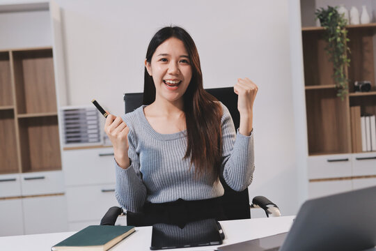 young woman is working on laptop in modern office environment, showcasing focused and productive atmosphere. She is dressed in professional white shirt, with coffee cup and small plant on table,