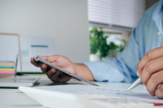 Businessman analyzing financial data on paper report and using digital tablet at office desk, concept of business strategy, investment growth, market research, and data analysis planning.