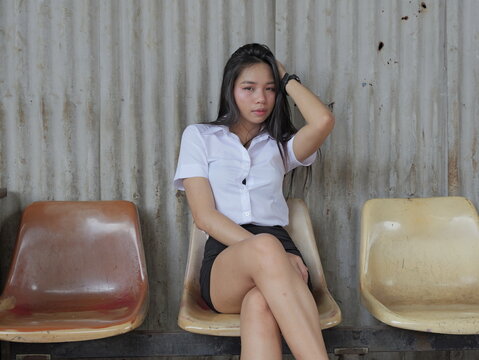 A young Asian woman with long flowing black hair, wearing a white short-sleeved collared shirt and black skirt, sits with her left hand gently threaded through her hair