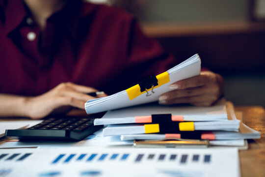 Business professional working on a laptop with financial charts, calculator, documents and coffee on a wooden desk, representing finance, accounting and office work.