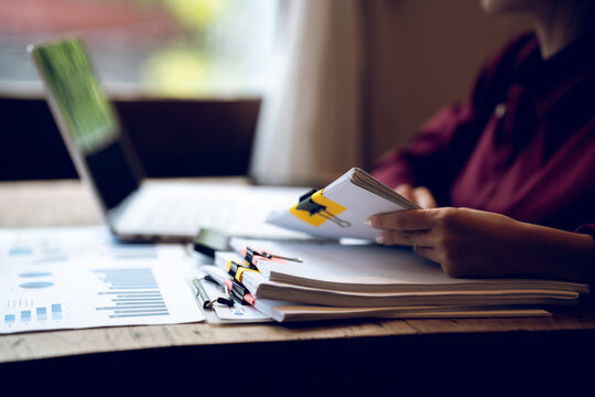 Business professional working on a laptop with financial charts, calculator, documents and coffee on a wooden desk, representing finance, accounting and office work.