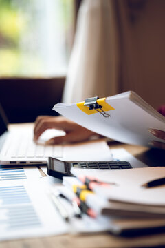 Business professional working on a laptop with financial charts, calculator, documents and coffee on a wooden desk, representing finance, accounting and office work.