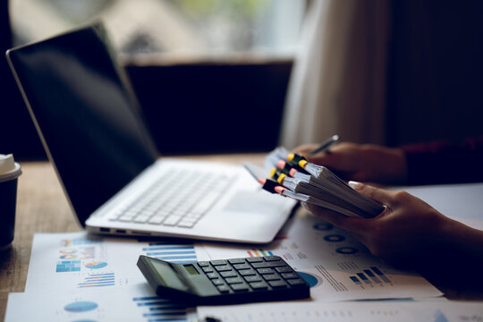 Business professional working on a laptop with financial charts, calculator, documents and coffee on a wooden desk, representing finance, accounting and office work.